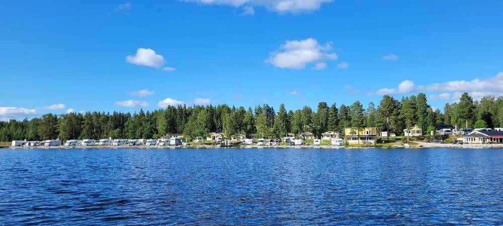 En naturskön vy över en vattenväg vid Kölåns stugby & camping, med lummiga stränder och stilla vatten, omgiven av grönskande landskap.