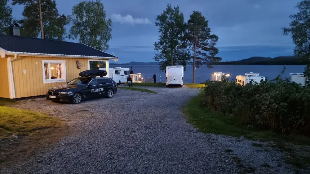 En naturskön utsikt över en stilla reservoar omgiven av frodiga skogar vid Kolgårdens stugby & camping. I bakgrunden syns en liten ö och en vidsträckt strand, vilket ger en rofylld atmosfär.