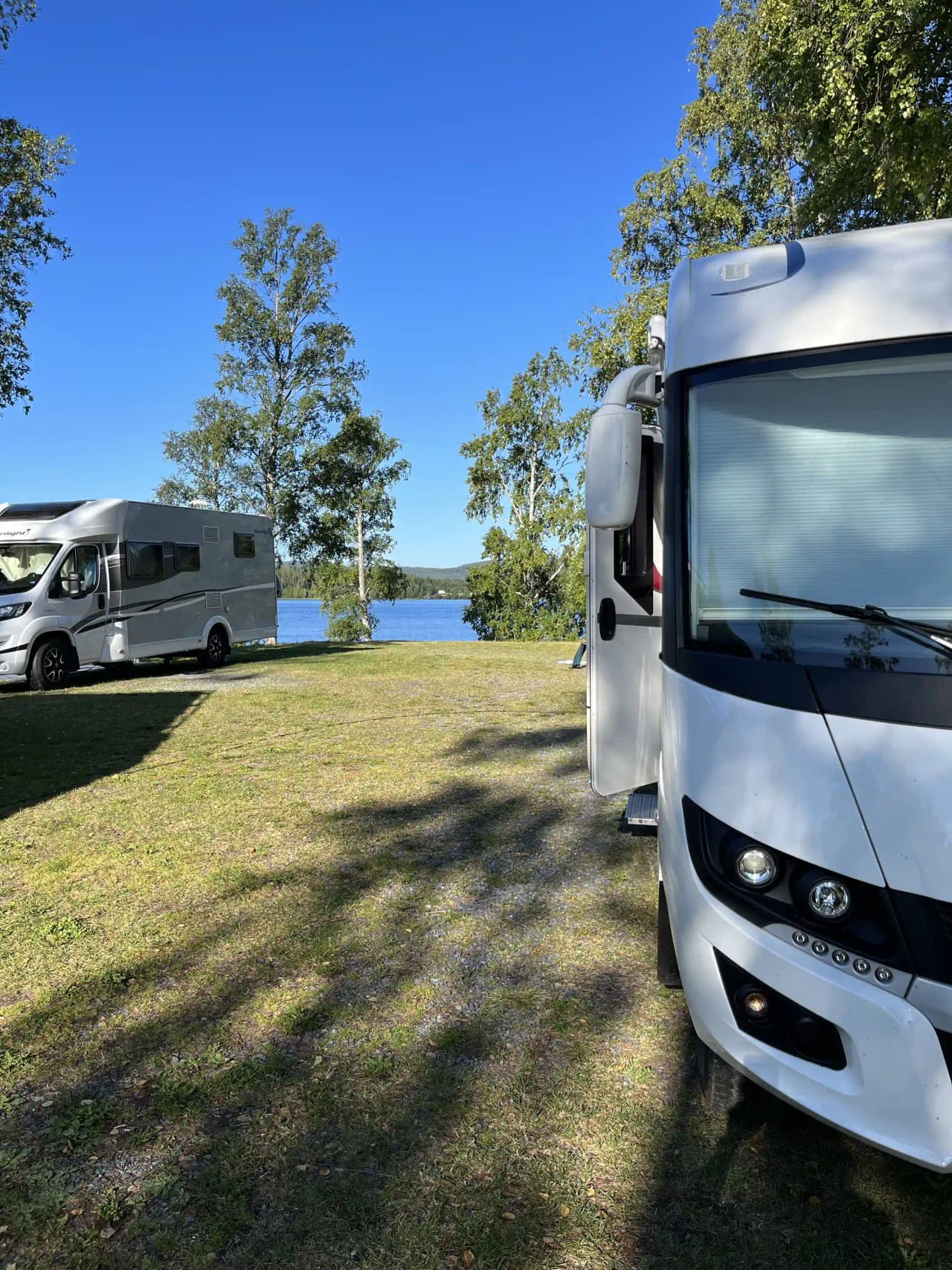 En husvagn och en husbil parkerade på en campingplats vid Snibbens Camping, med träd och en skog i bakgrunden.