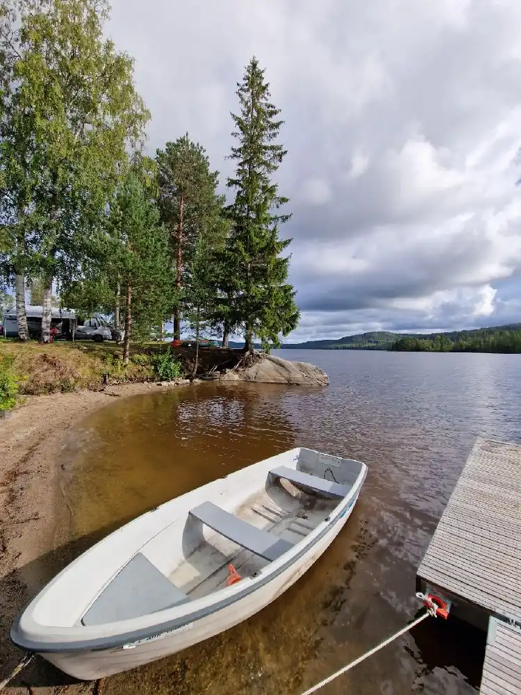 Alt-text: En motorbåt är förtöjd vid en liten brygga vid Snibbens camping, omgivet av stilla vatten och grönskande landskap.