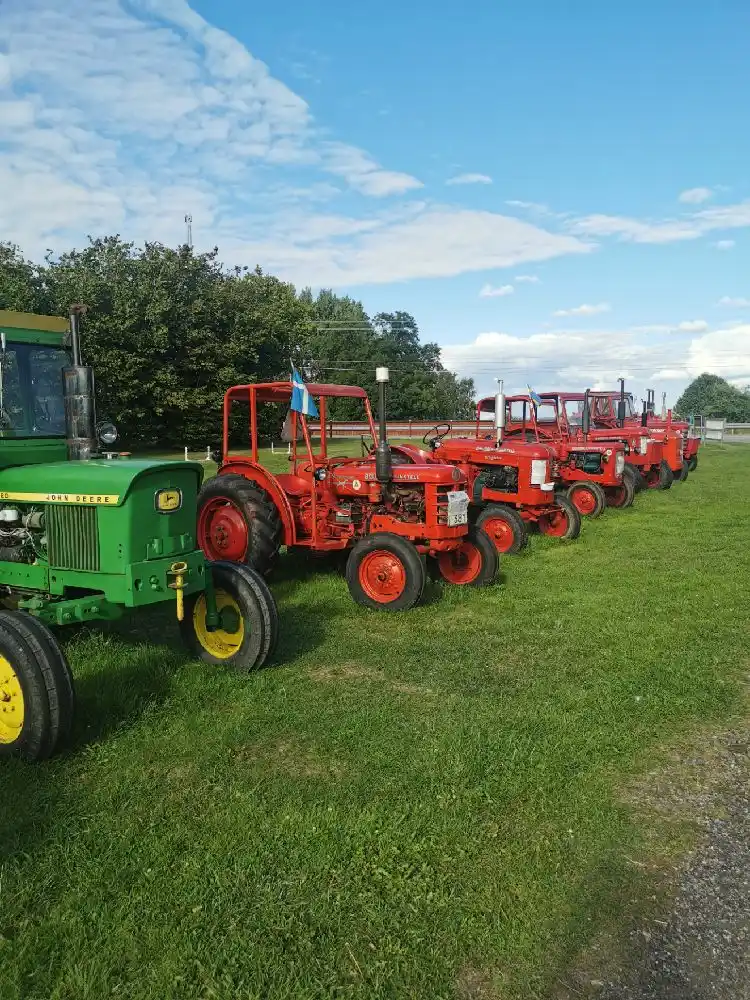 En traktor med stora däck står på ett fält vid Gripenbergs gård, omgiven av jordbrukslandskap.