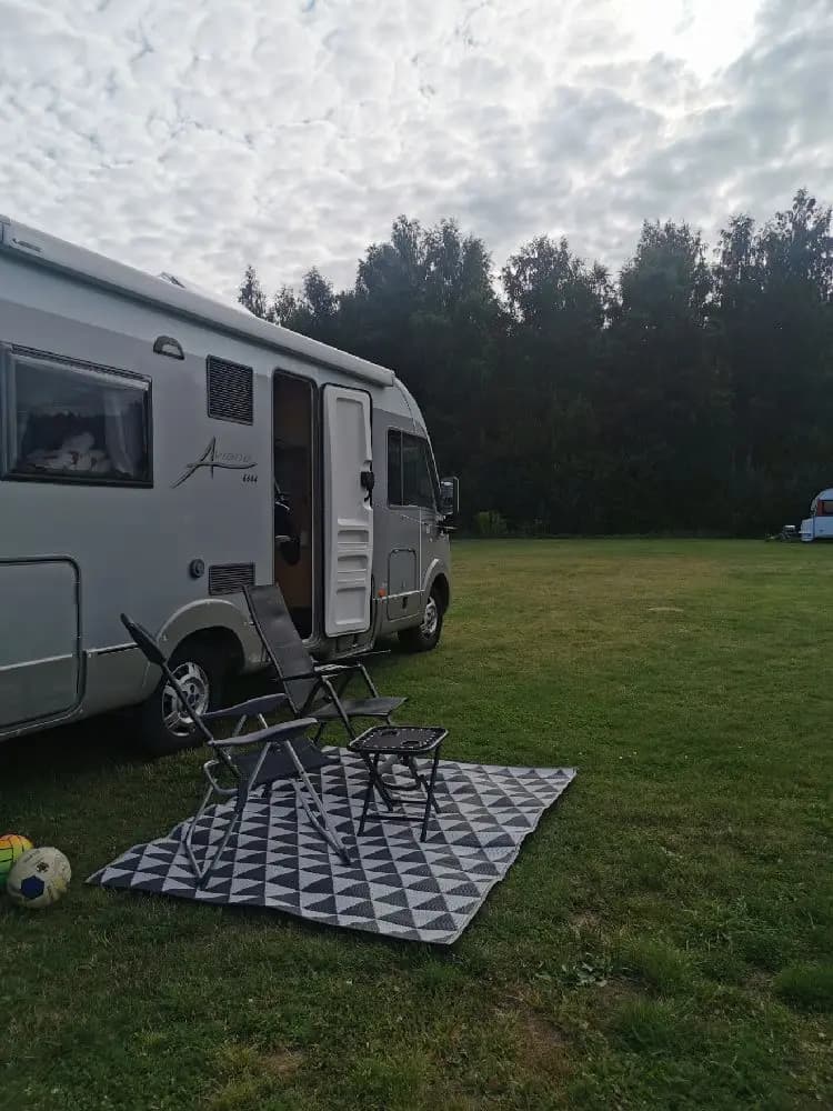 En grön gräsmatta där en husvagn och en campervan står parkerade vid Gripenbergs gård, omgivna av träd i en lummig parkmiljö.