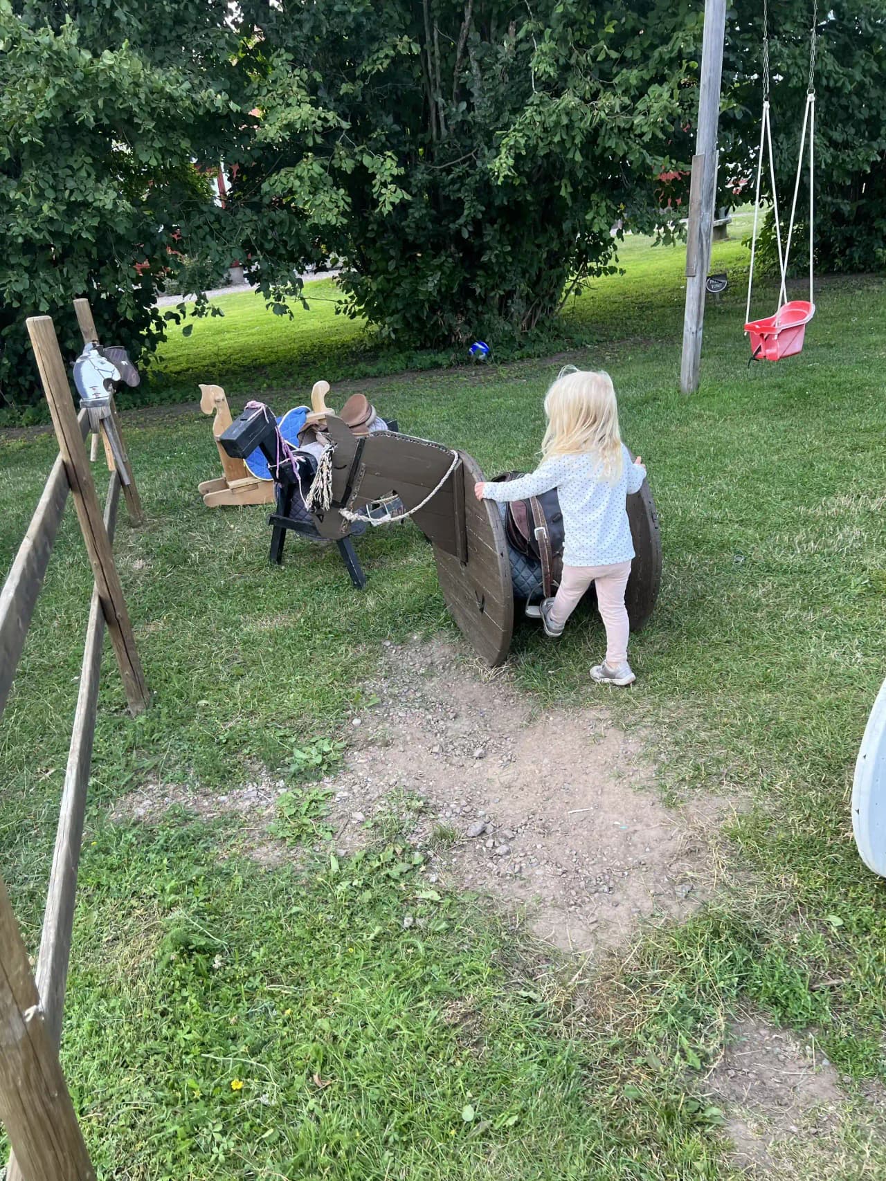En grupp småbarn leker glatt på en grön gräsmatta vid Gripenbergs gård, omgiven av sommarens frodiga natur, vilket skapar en härlig atmosfär för familjesemester och avkoppling.