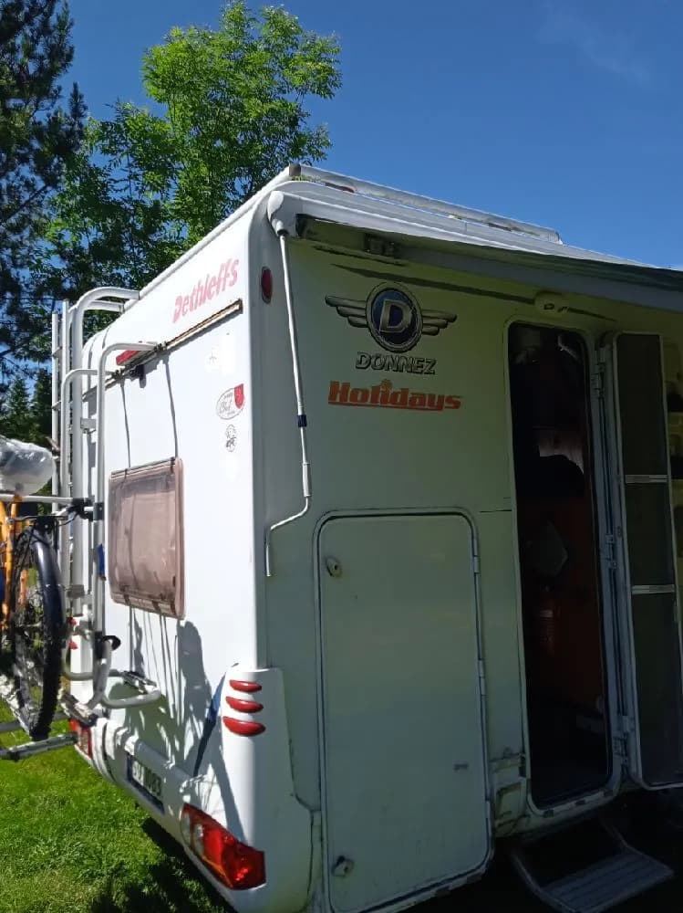 En campingplats med flera husvagnar och husbilar uppställda på gräsytor, omgivna av träd och natur, vid Lesjöbyns camping.