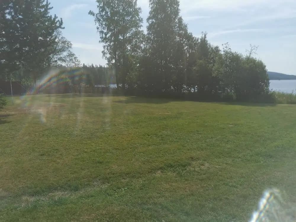 En somrig bild av Lesjöbyns camping med blå himmel och gräsfält som sträcker sig under vita moln. En lugn äng med grönt gräs breder ut sig i förgrunden.