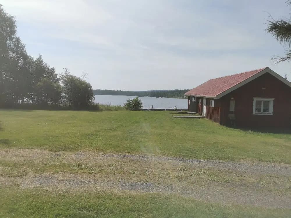 En pittoresk stuga vid en grönskande gräsmatta nära ett vattenreservoar i Lesjöbyns campingområde.