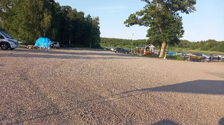 En bild av en parkering vid södra Kinda båtklubb, där flera olika typer av bilar står parkerade, inklusive lyxfordon, familjebilar och SUV:ar.