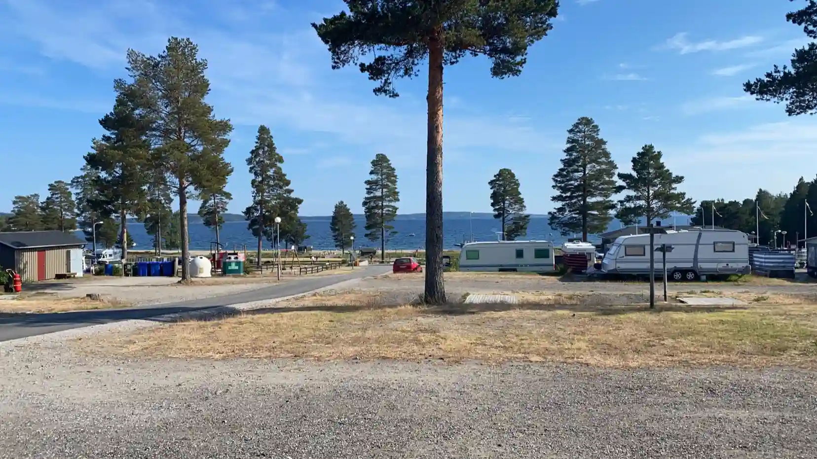 En pittoresk kustlinje med en sandig strand vid Gullviks Havsbad Camping & Stugby, omgiven av frodig grönska och ett lugnt hav i bakgrunden.