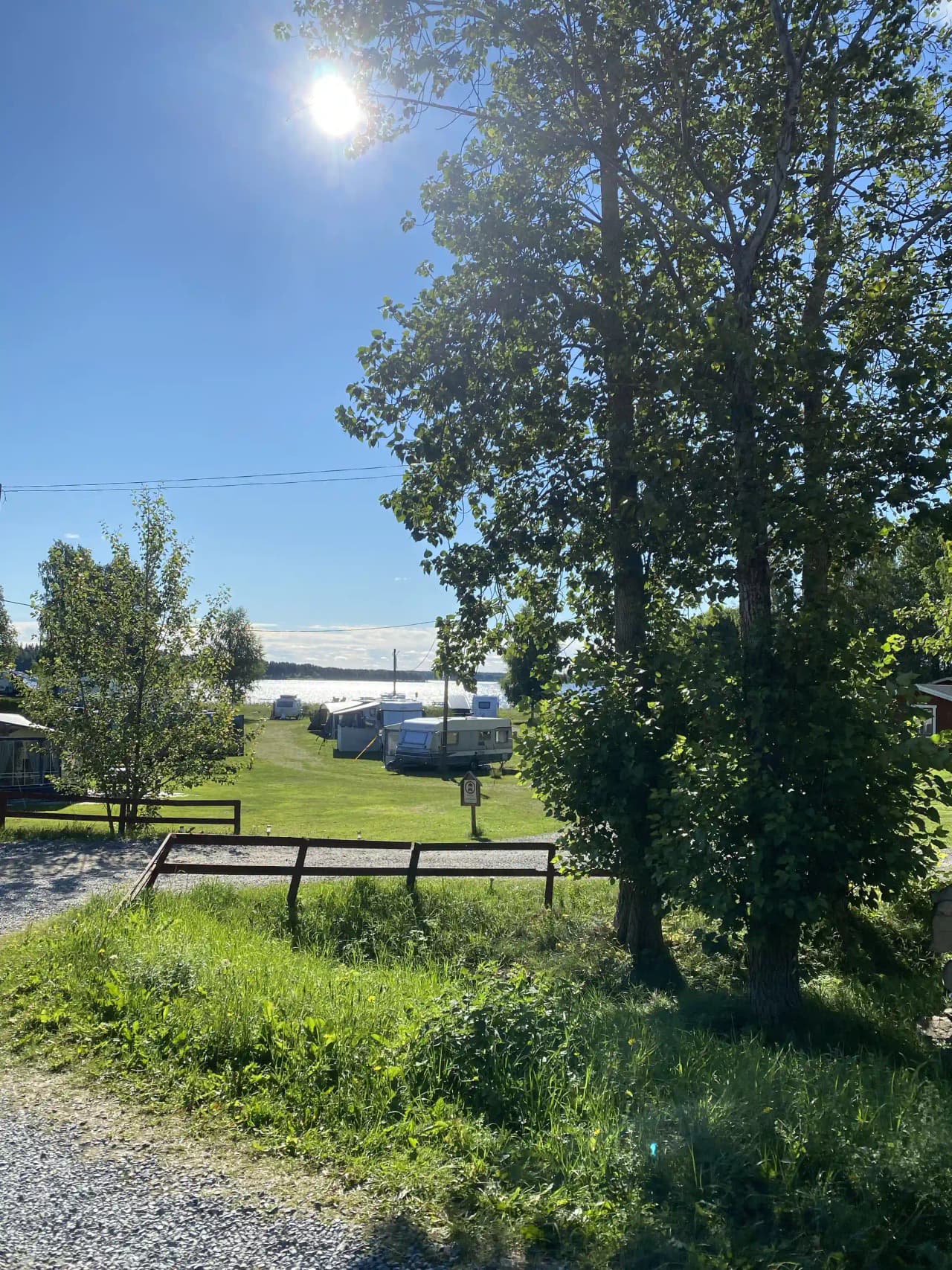 En grön campingplats med gräsmatta, parkerade husbilar, och skuggade områden vid Falkudden camping, café och stugby.