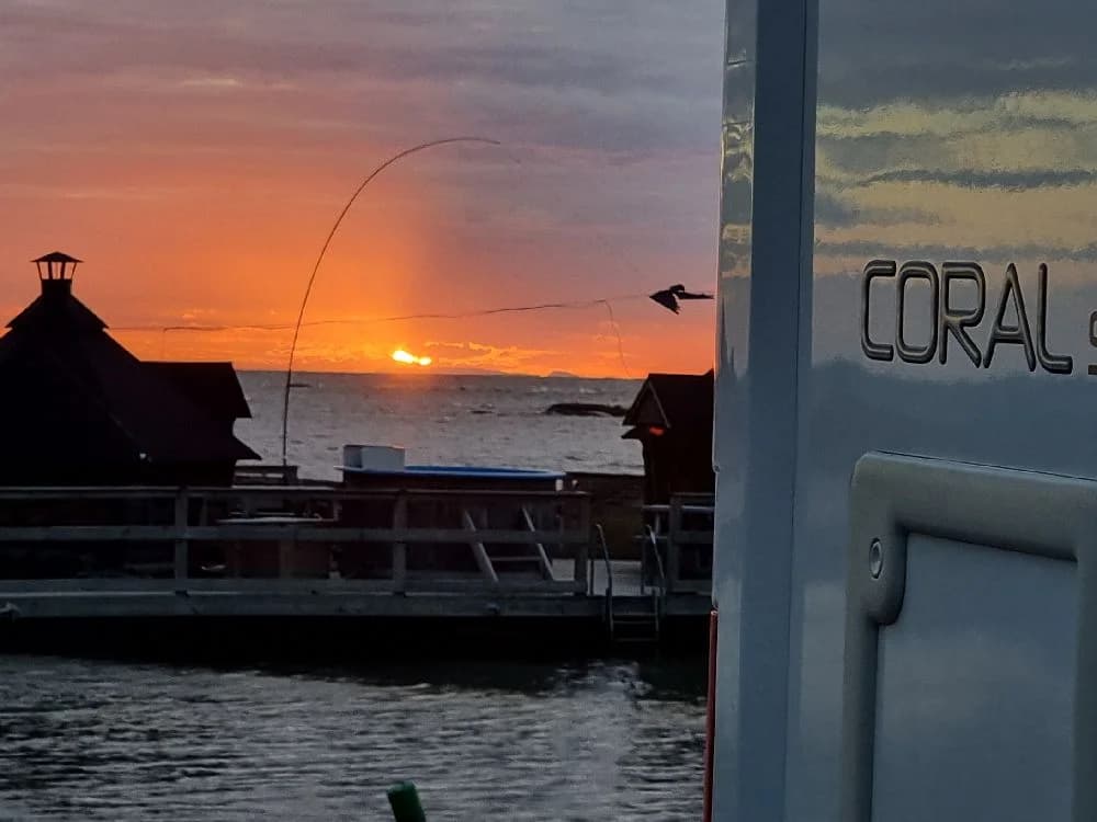 En siluett av en båt vid solnedgången på Filsbäcks camping, med ett glödande efterljus över havet i skymningen.