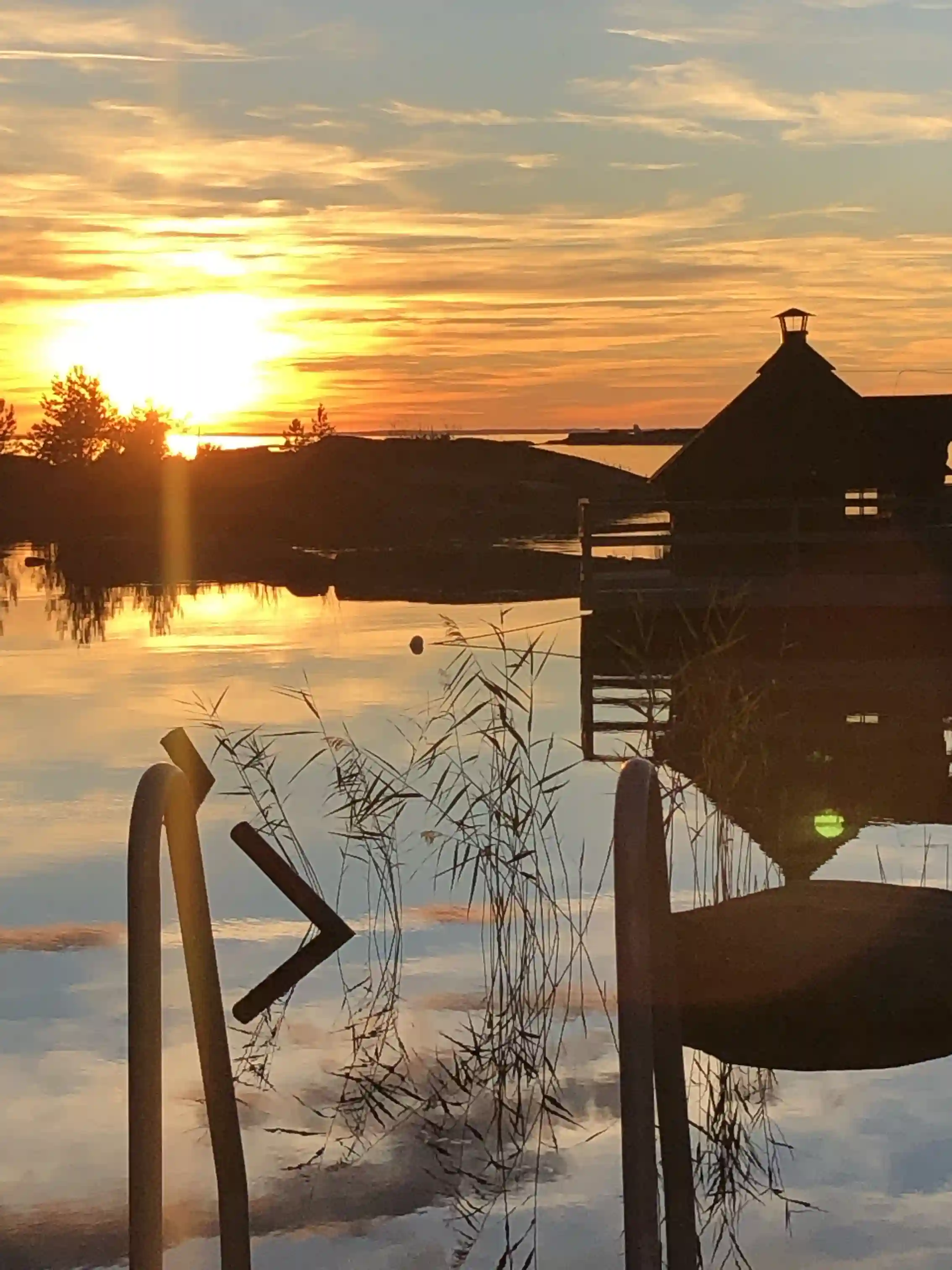 Vy över Filsbäcks camping vid solnedgången. Vattnet speglar himlens färger medan horisonten går in i skymning, vilket skapar en lugn och naturnära atmosfär.
