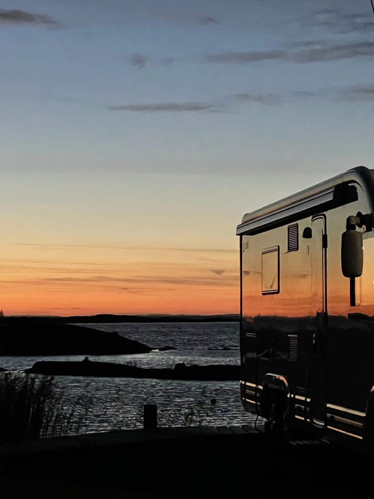 En husbil parkerad vid Filsbäcks camping i skymningen, omgiven av en vacker solnedgång vid horisonten.