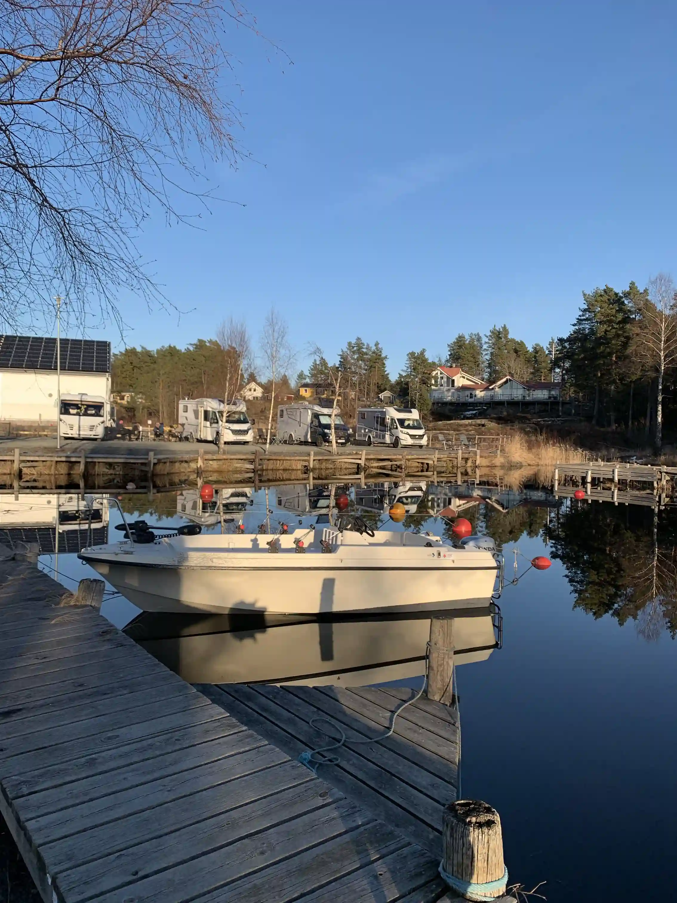 En liten marina vid Filsbäcks camping med flera förtöjda motorbåtar vid en brygga, omgiven av stilla vatten och en klar himmel.