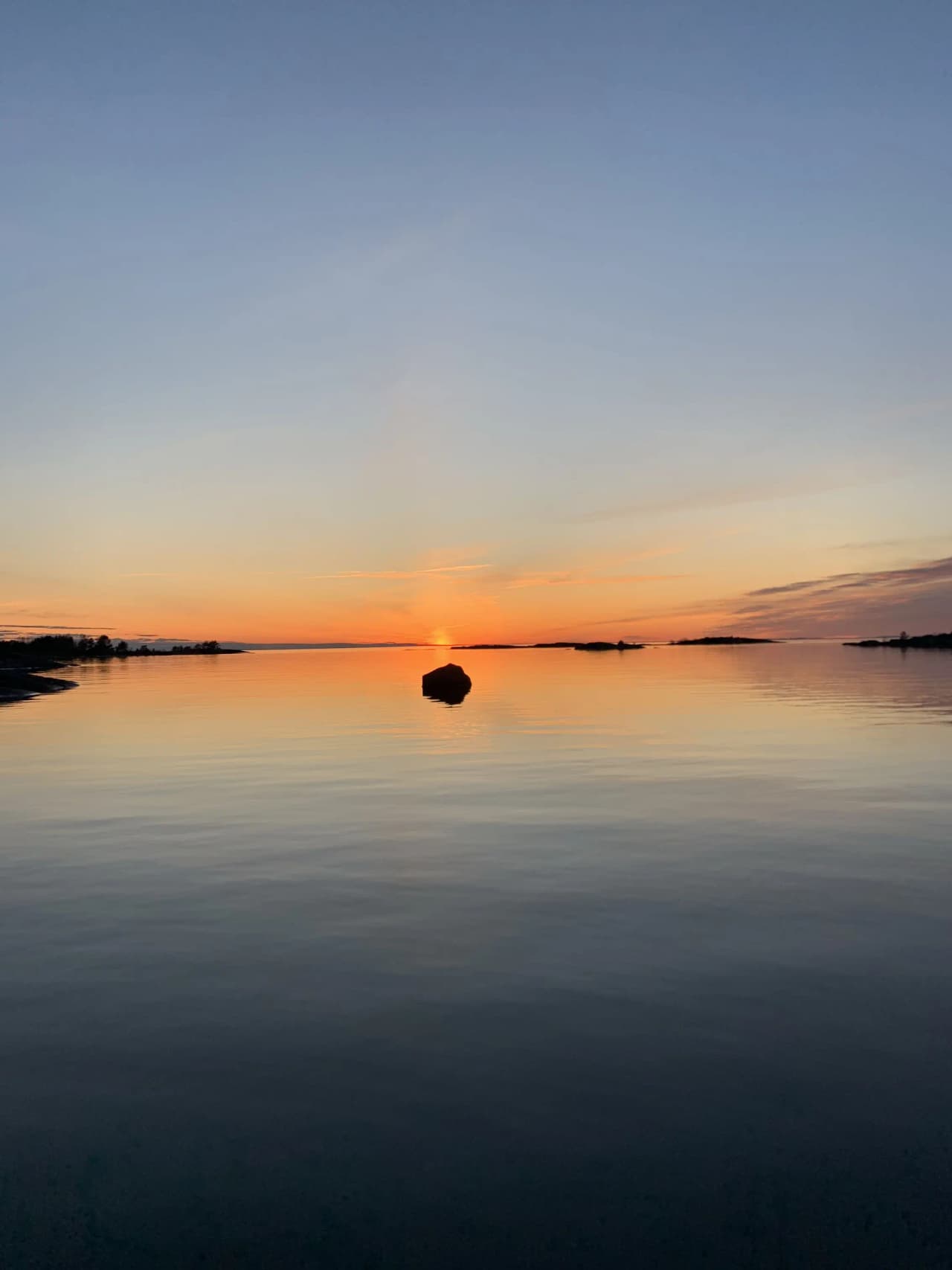 En vacker solnedgång vid Filsbäcks camping med en blå himmel och vattenhorisont, där kvällens ljus skapar ett gyllene glöd över de tysta molnen och reflekteras i det lugna vattnet.