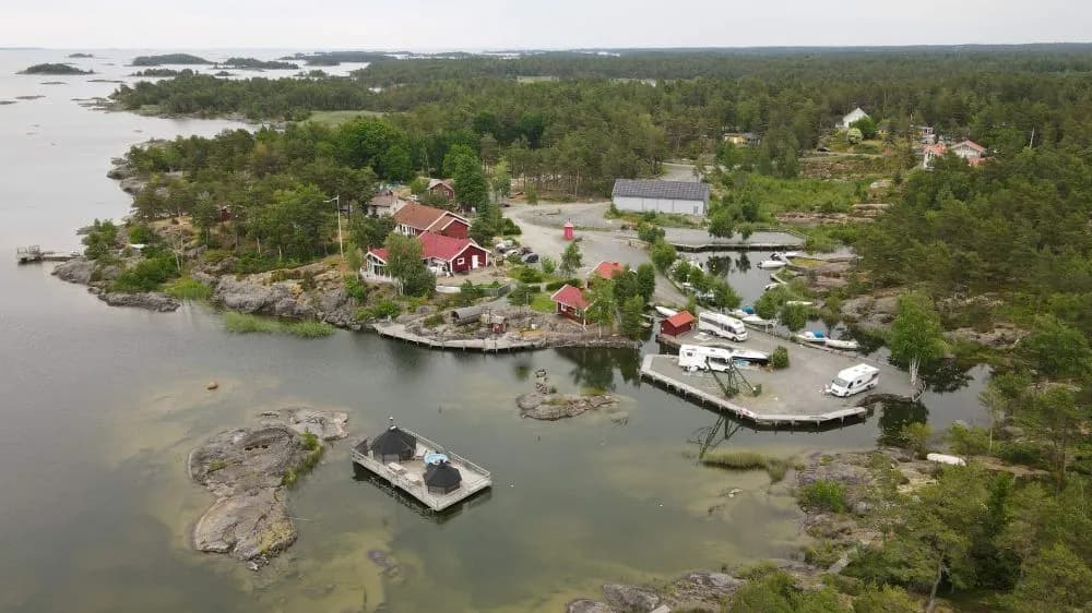 Luftfoto över Filsbäcks camping, visar en fågelperspektivvy av området med flodlandskap, stugor och en flod eller kanal som flyter genom en by.