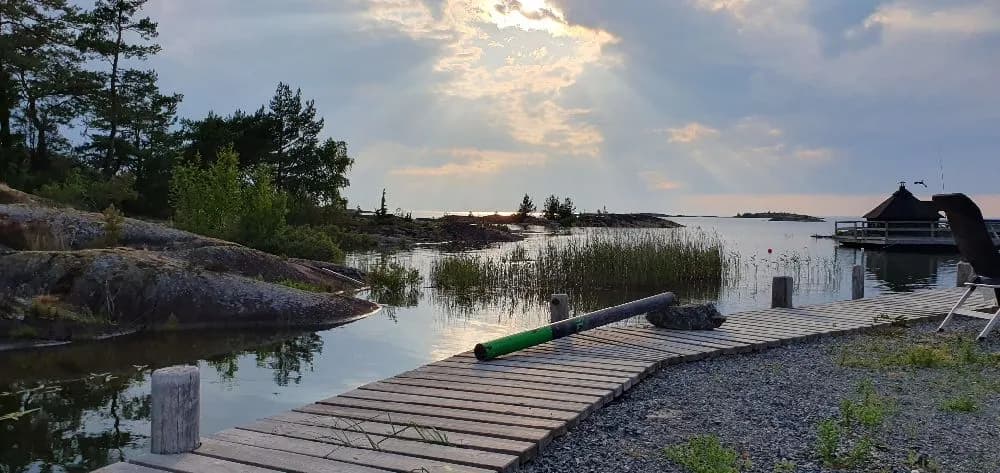 En solig dag vid Filsbäcks camping med en vy över en sjökant, brygga och omgivande våtmarker.