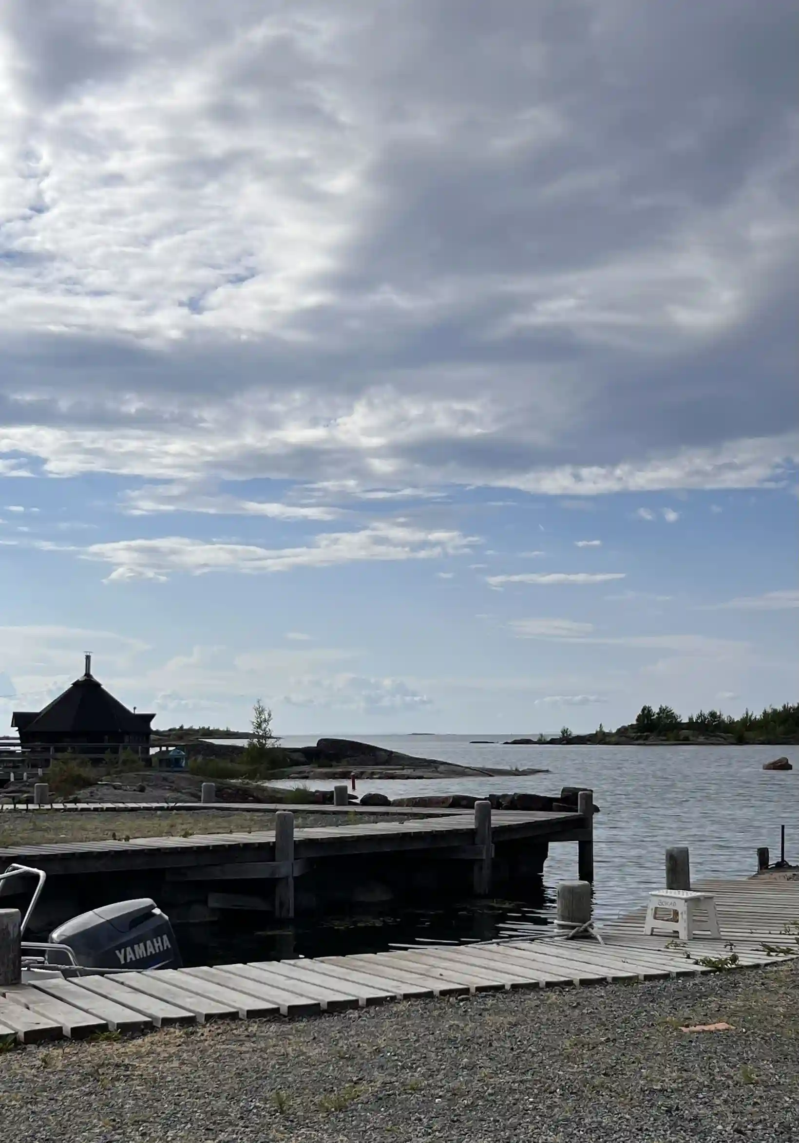 En naturskön vy över Filsbäcks camping med en molnig himmel och en glittrande sjö längs kusten.