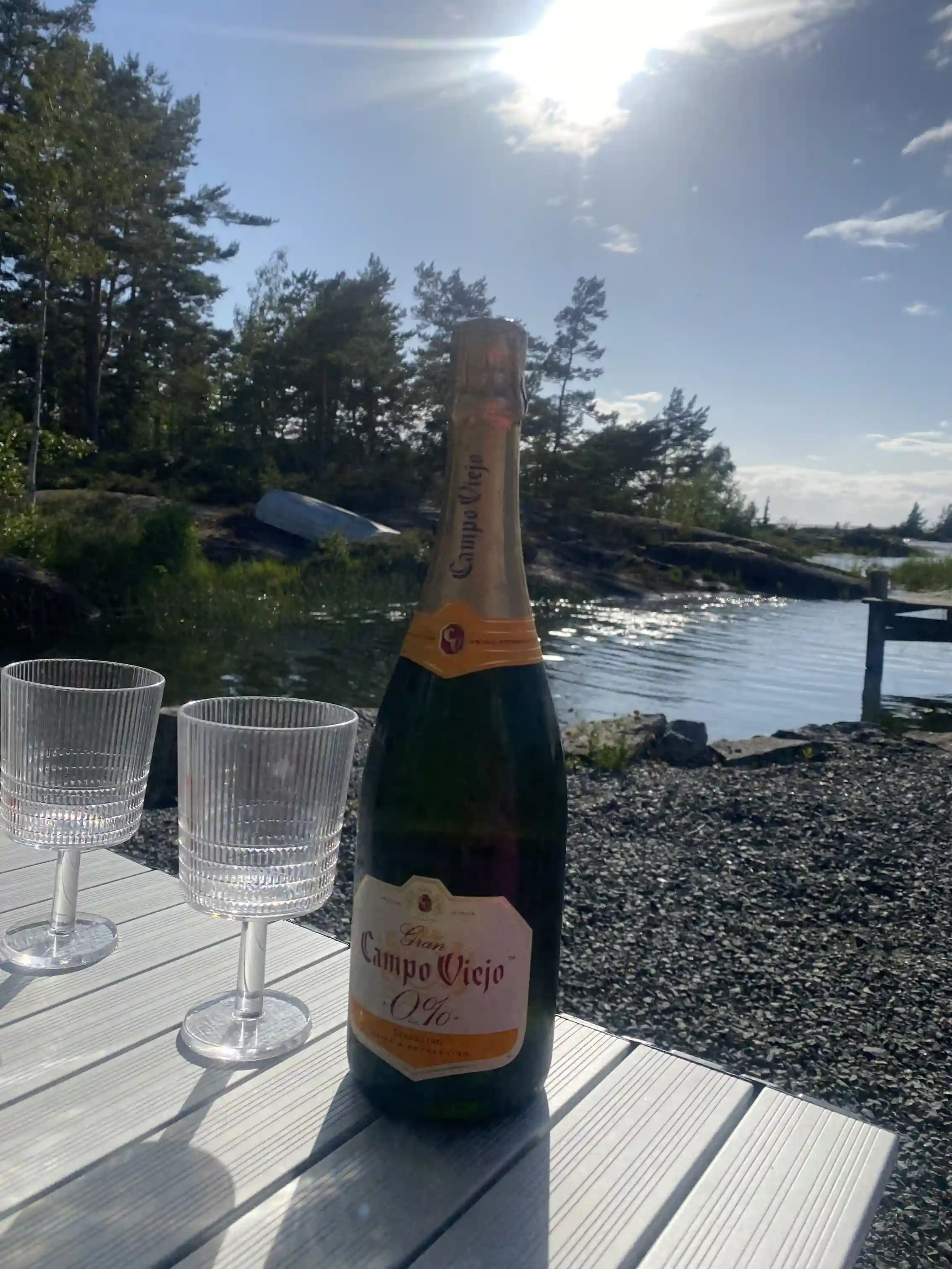 En uppdukad campingbord med flera olika spritflaskor och glas, redo för servering. Flaskorna innehåller olika sorters alkoholhaltiga drycker, och glasen står framme för servering. Bakgrunden är suddig, vilket ger ett intryck av social samvaro.