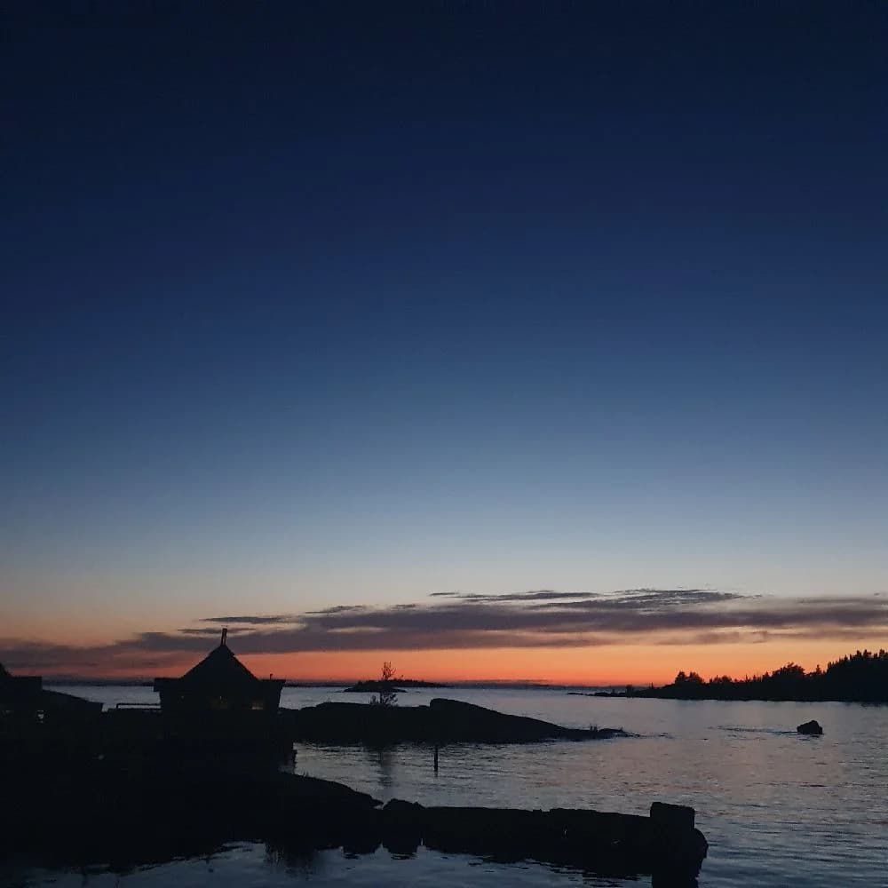 En vacker solnedgång över vattnet vid Filsbäcks camping, med en klarblå himmel och en mjuk horisont i bakgrunden.