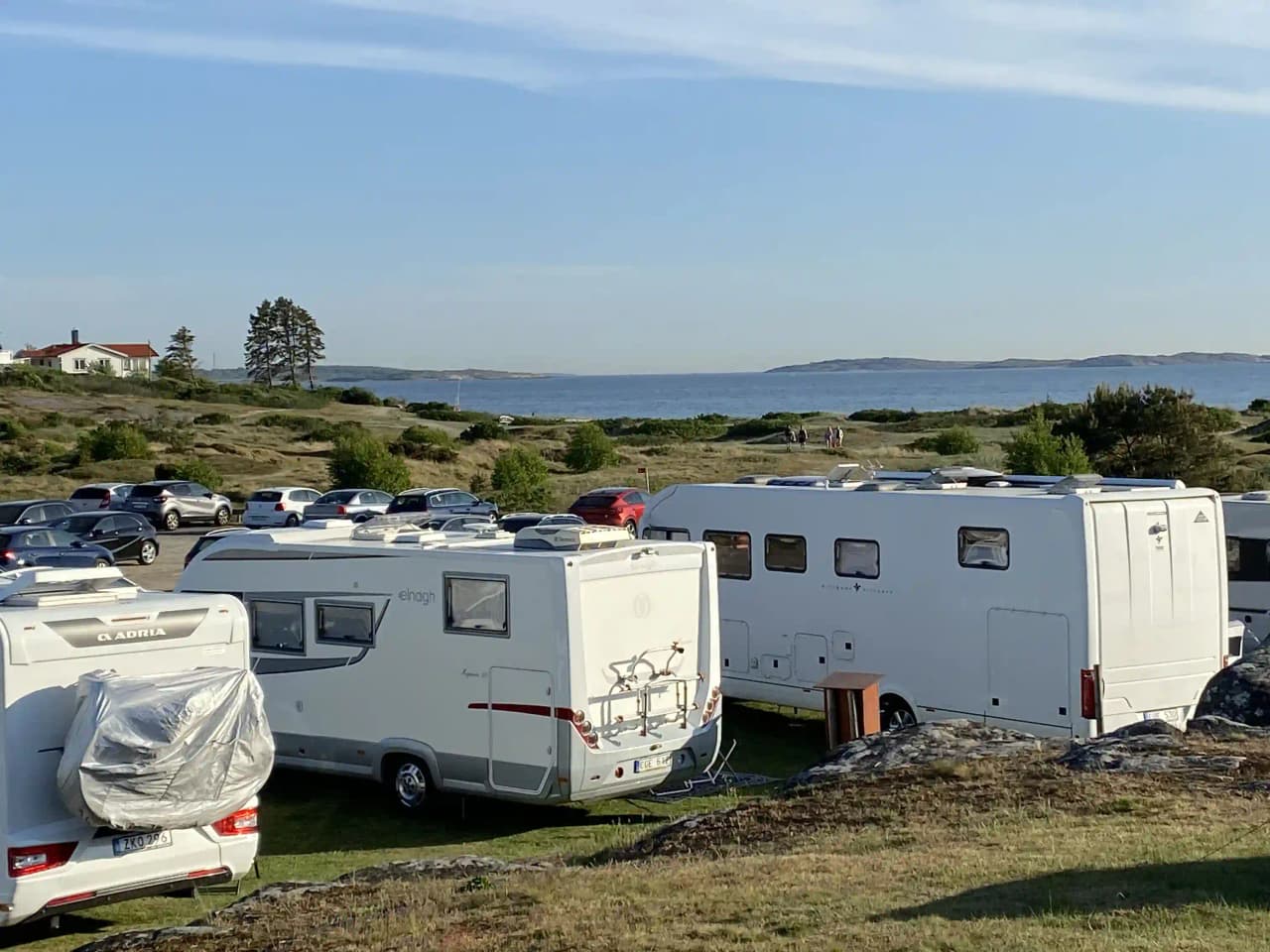 En husbil och en husvagn parkerade på en campingplats vid Åsa Camping & Havsbad, omgiven av andra fordon och en parkering.