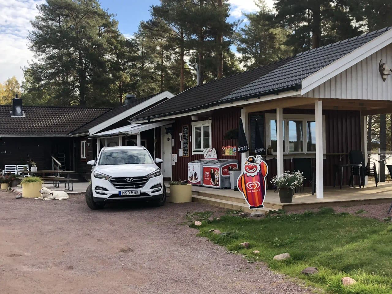 Ett pittoreskt hus vid Våmåbadets camping omgiven av en grönskande trädgård. På uppfarten står en lyxig bil parkerad.