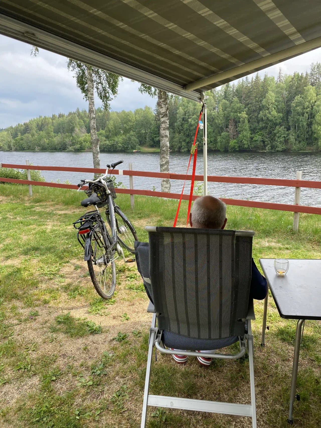 En solig dag vid Grebbestadfjorden med utemöbler och en cykel i förgrunden, omgivna av skuggor från träden.