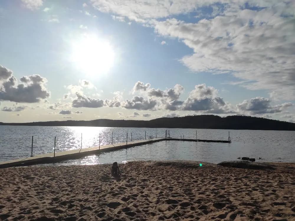 Vy över en solig strand vid Lövekulle camping, med klart vatten och en horisont som möter den blåa himlen.