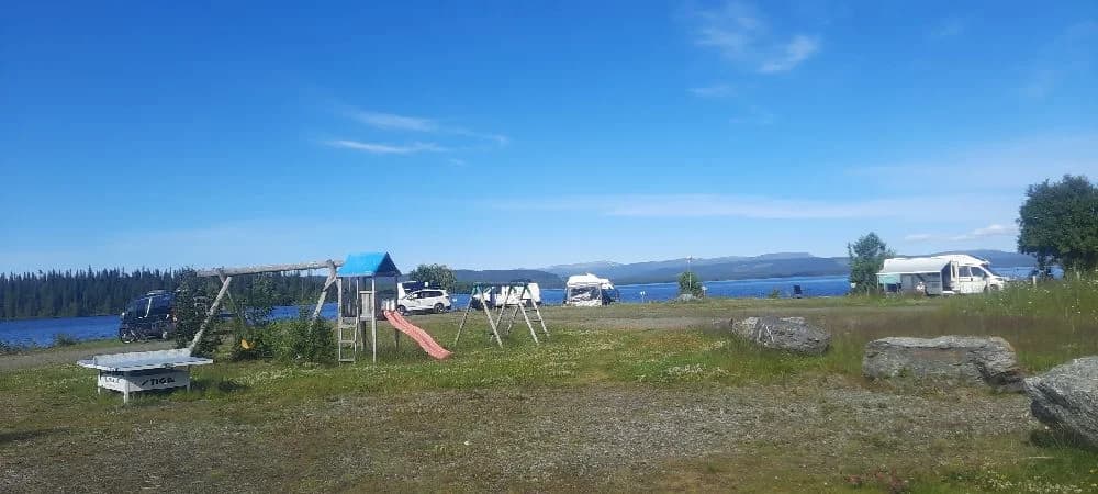 En campingplats med tält och mindre husbil under en blå himmel med några moln.