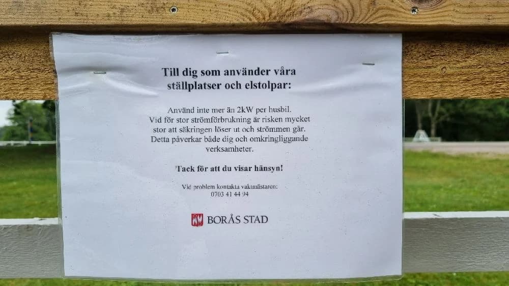 En grönskande gräsmatta omgiven av parkväxtlighet vid Hofsnäs herrgård, med en skylt som markerar platsen.