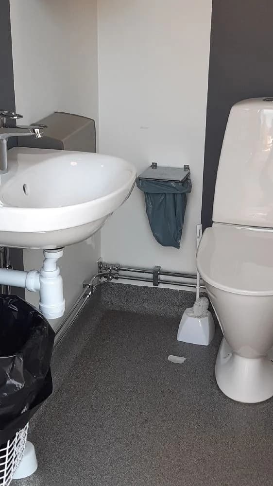 En vit, klassisk toalettstol med matchande handfat syns i ett kaklat badrum, omgärdat av kakelgolv. Rummet är rent och stilrent inrett.