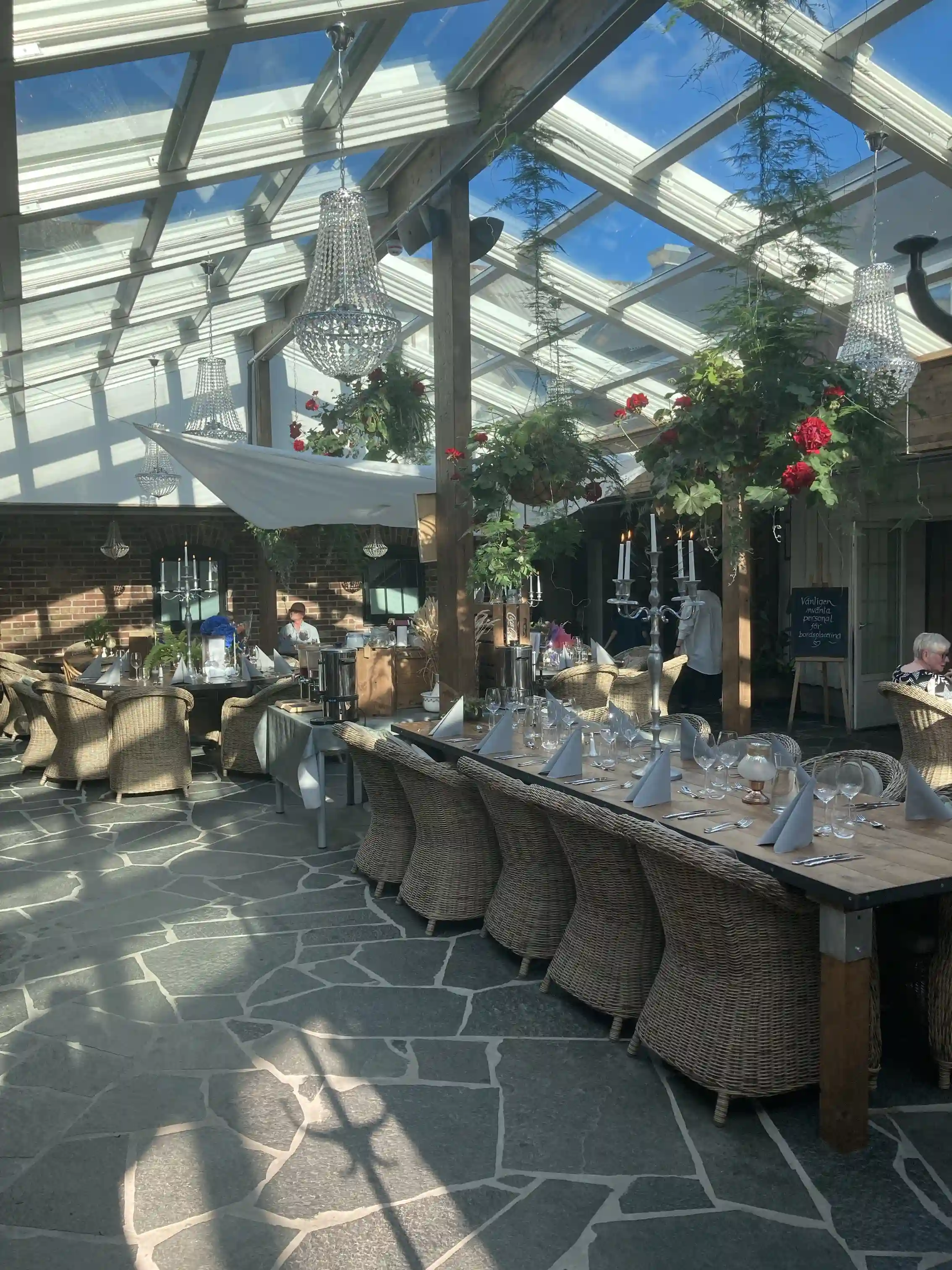 Utomhusmiljö vid Lögnäs Gård med bord och stolar under en skuggande struktur. Blomkrukor och husväxter pryder området, vilket ger en avkopplande atmosfär för gäster som besöker detta hotell och spa.