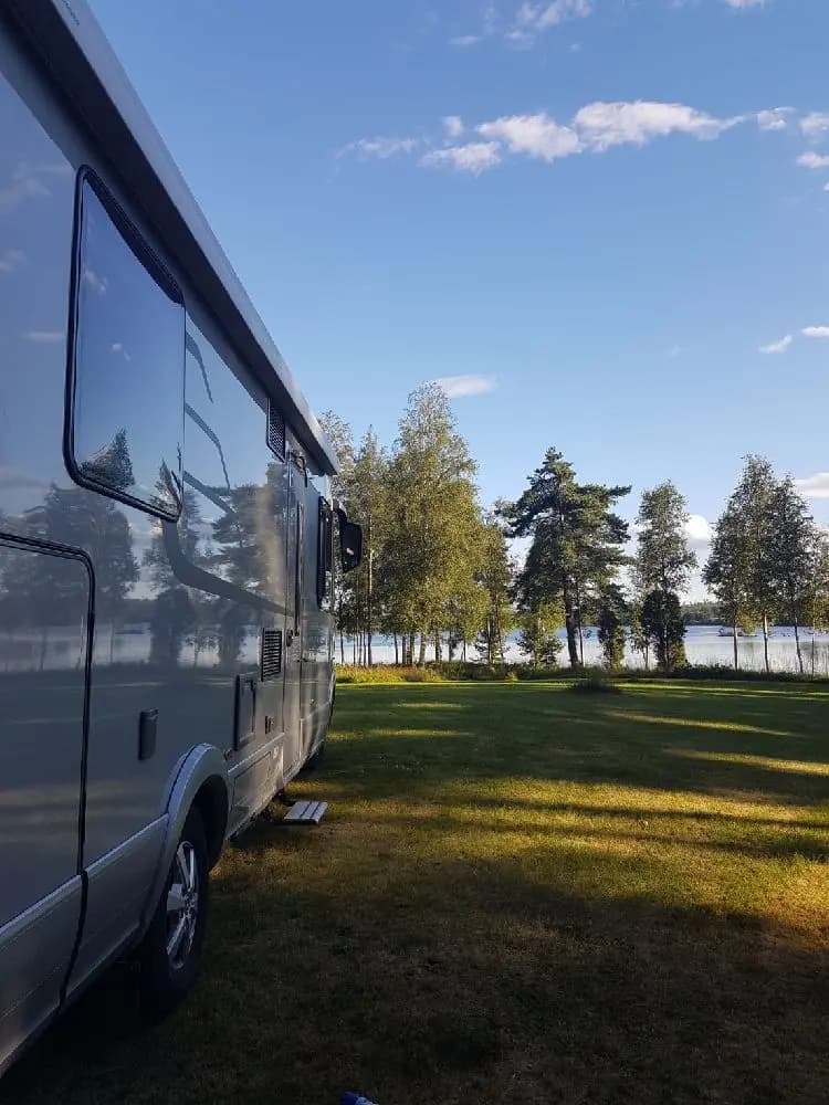En husvagn parkerad på en grön gräsmatta vid Moarps B&B, omgiven av träd och en lugn parkmiljö.