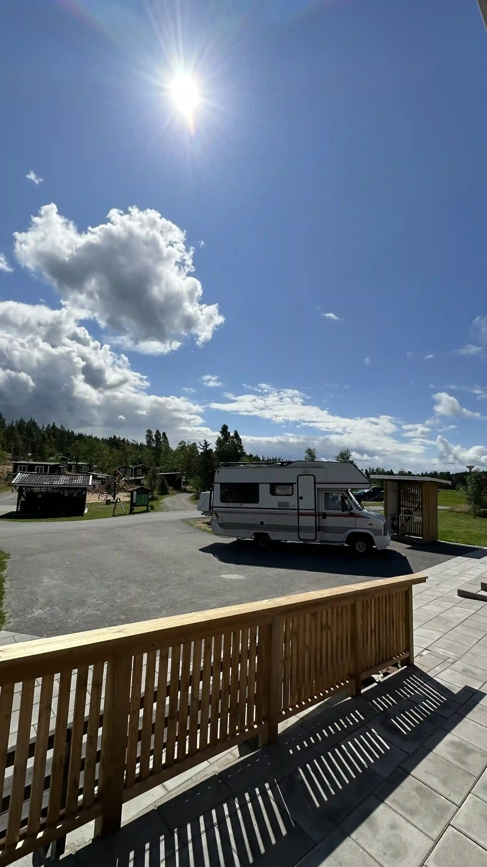 En husbil och husvagn parkerade på en grusväg vid Hoks naturcamping, omgivna av gröna träd och under en himmel med cumulusmoln.