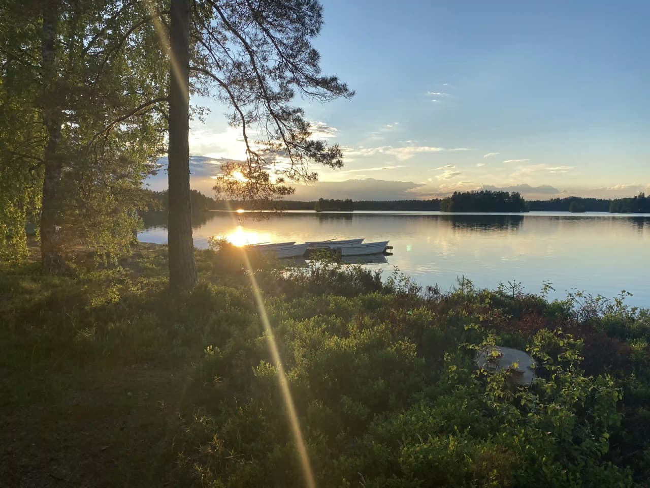 En lugn sjö vid Orrefors camping under skymningen, med en klarblå himmel och naturskön horisont.