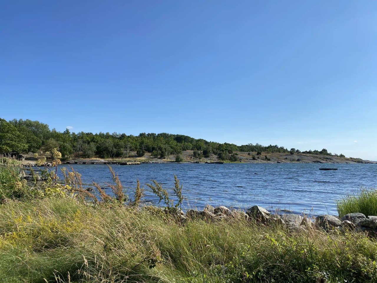En naturskön vy vid Stenbräckagården Hägnan med blått vatten som sträcker sig längs kusten, omgiven av frodig grönska och naturliga landformer.