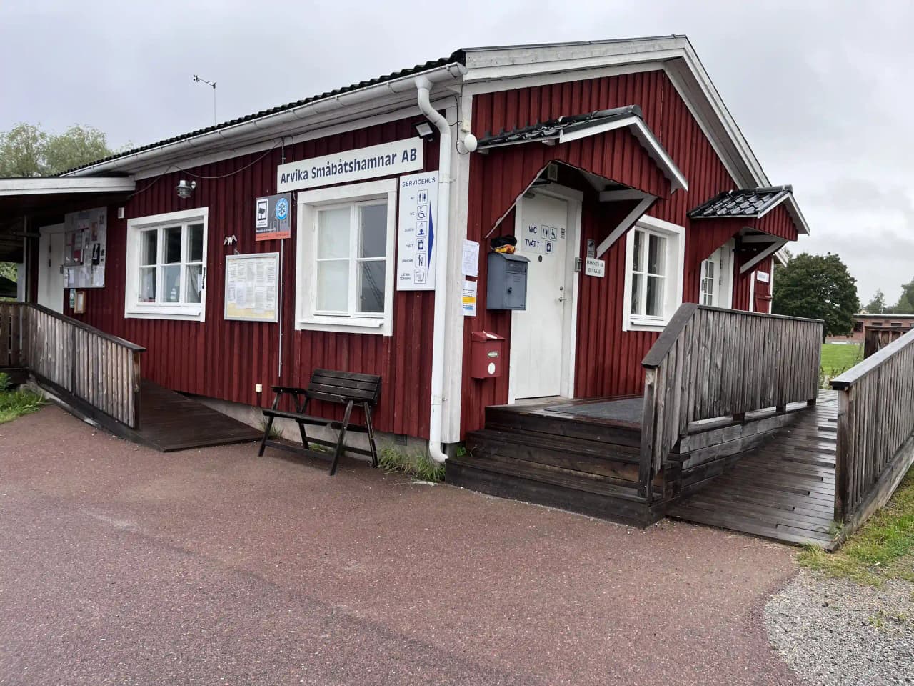 En träport vid Arvika småbåtshamn, omgiven av båthus och vatten, som skapar en inbjudande entré till hamnområdet.