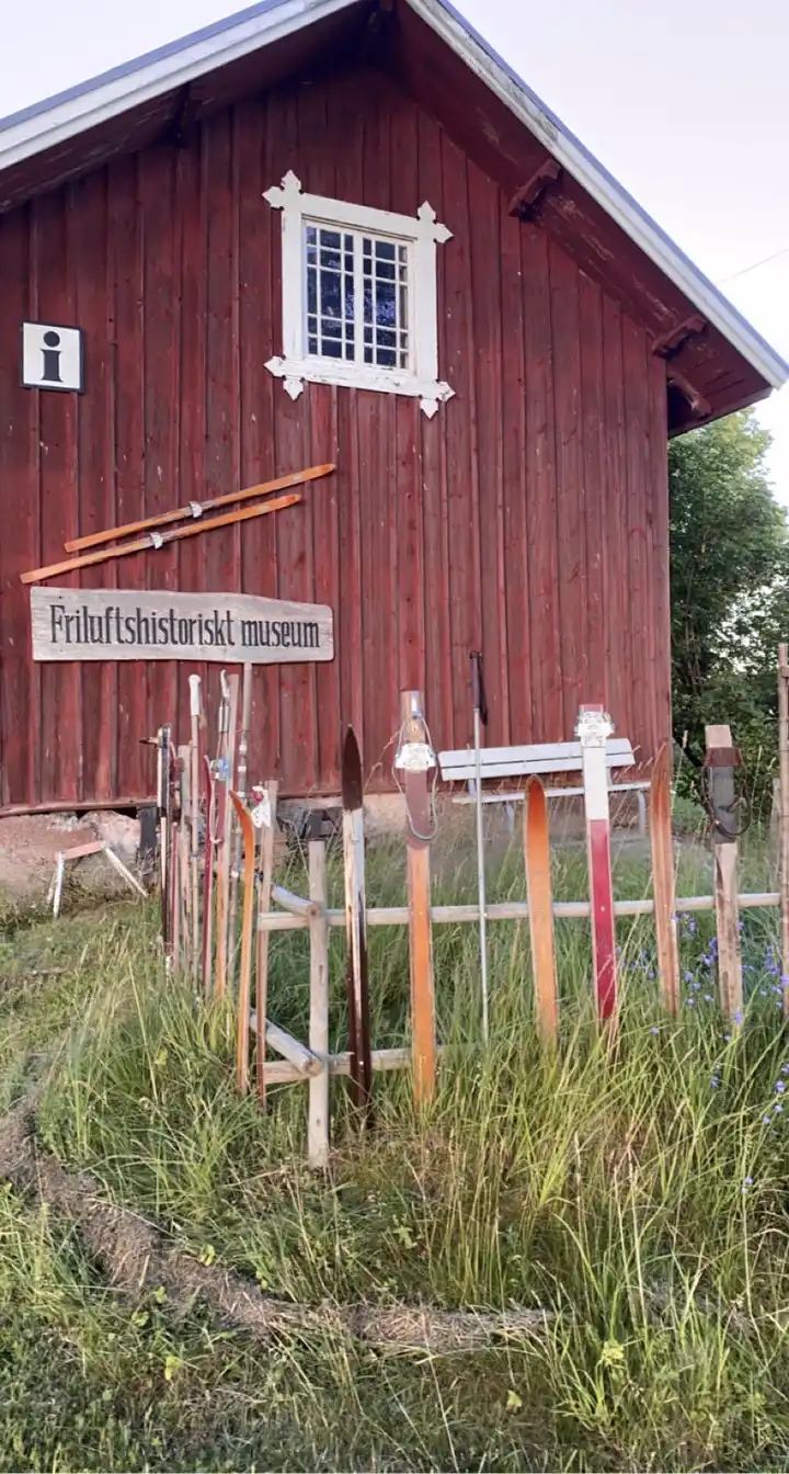 Ett träbeklätt fritidshus på Gustavsvik Resort, med en dörr och fönster, omgiven av grönska och trädgårdselement.