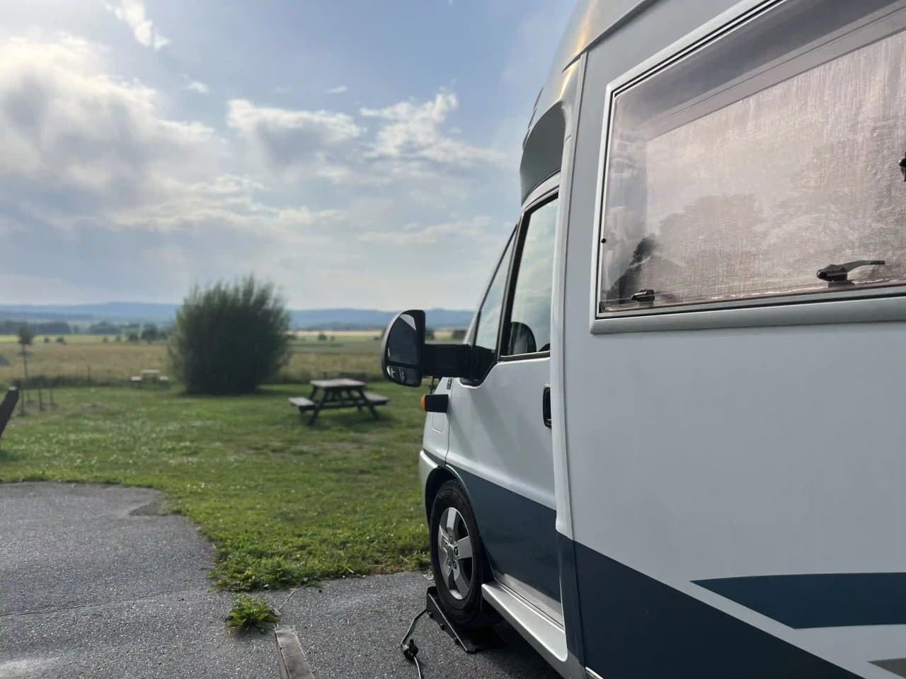 Bild av en husbil och en minibuss parkerade bredvid varandra vid Gustavsvik Resort, omgivna av grönska och en campingmiljö.