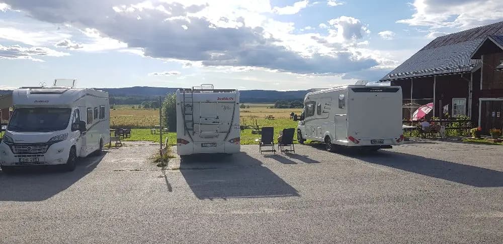 En husbil och flera fordon står parkerade på en plan under en molnig himmel vid Gustavsvik Resort.
