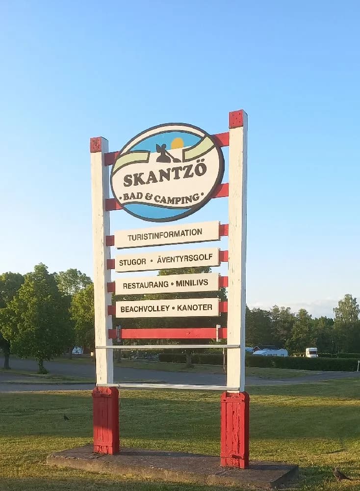 En informationsskylt vid Skantzö Bad & Camping, med stolpar som stödjer den och inslag av reklamelement.