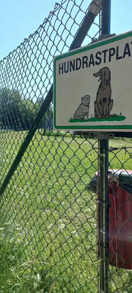 Bild med kedjelänkstaket och skylt i förgrunden, vilket skapar en inhägnad känsla vid Skantzö Bad & Camping. Staketet avgränsar ett grönt område vilket är del av campingplatsens faciliteter.