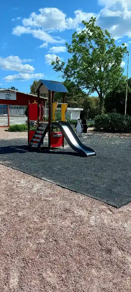 En lekplats med rutschkana och annan utomhuslekutrustning på Skantzö Bad & Camping, omgiven av grönska och skuggade områden.