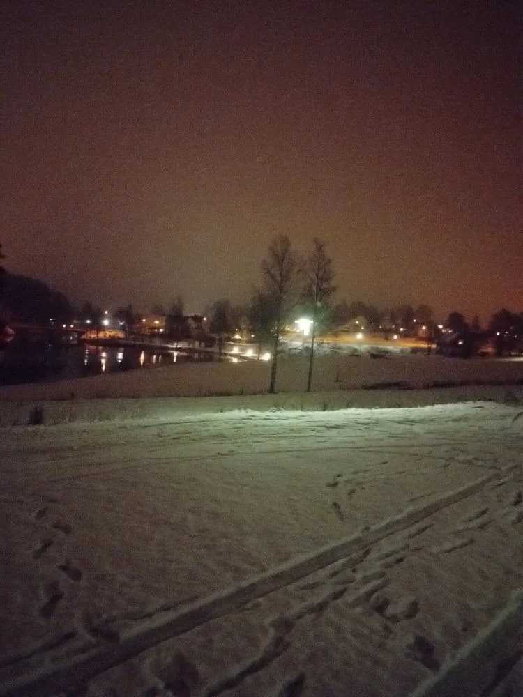 En nattbild av Bygdsiljums camping där snön lyser upp landskapet. Gatlyktor kastar ett varmt sken över den frusna marken i den tysta vinternatten.