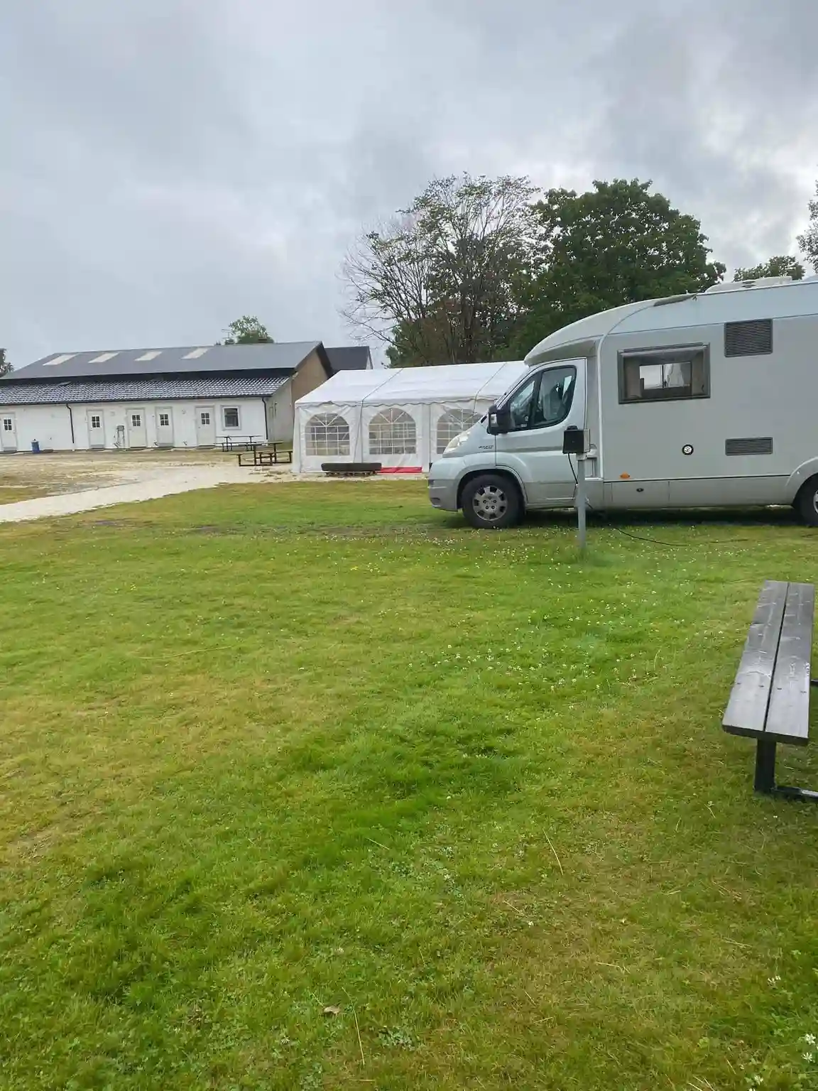 Bild av Kerstins camping: En rymlig campingplats med grön gräsmatta och flera parkerade husvagnar och bilar. Flera platser upptagna av personbilar och husvagnar som står parkerade på en planerad parkeringsyta. Campingen omges av träd och grönska, vilket skapar en lugn och naturnära atmosfär.