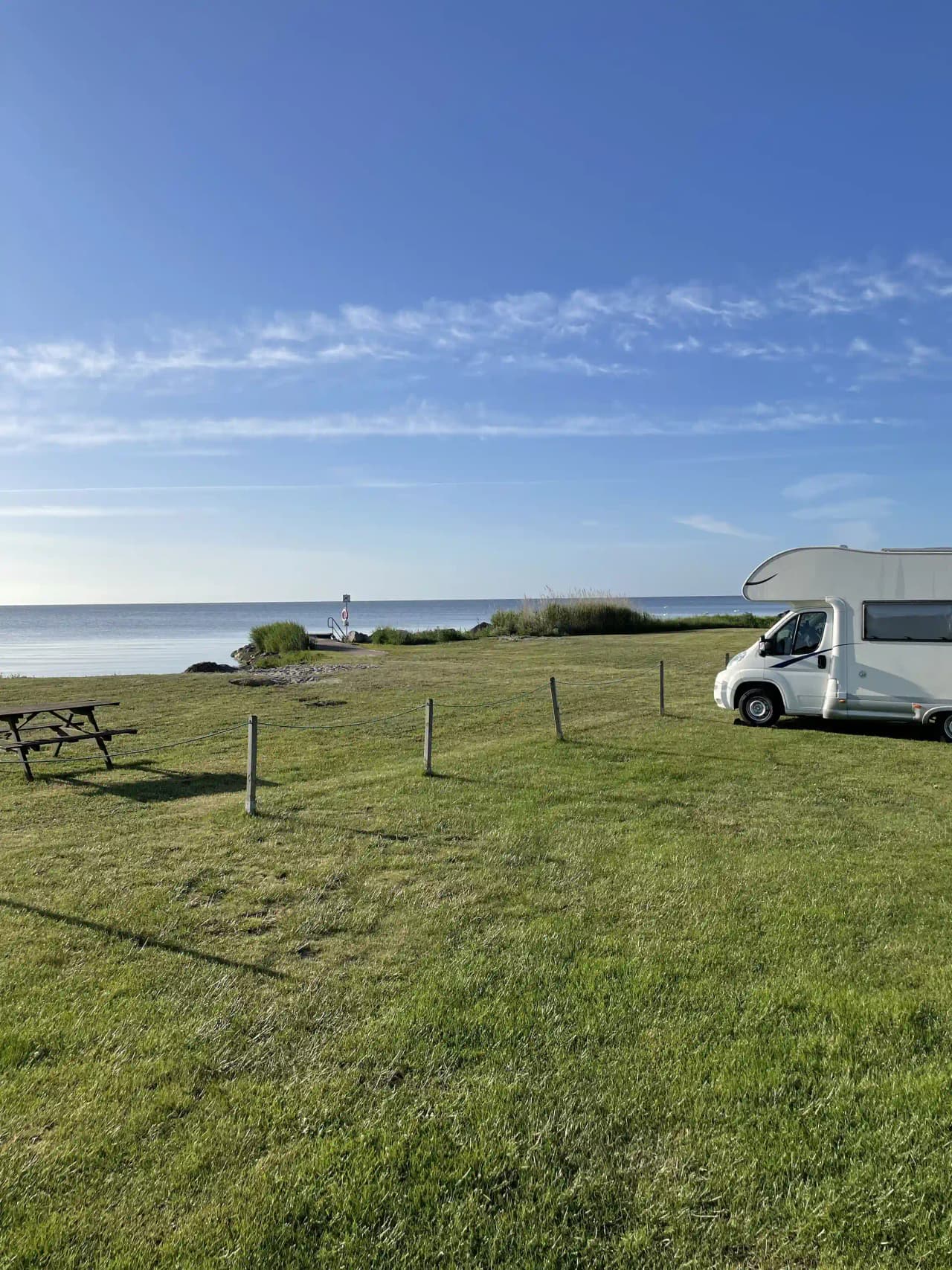 En husbil och husvagn parkerade på en grön campingplats vid Björkenäs Camping, med skog och grönska i bakgrunden.
