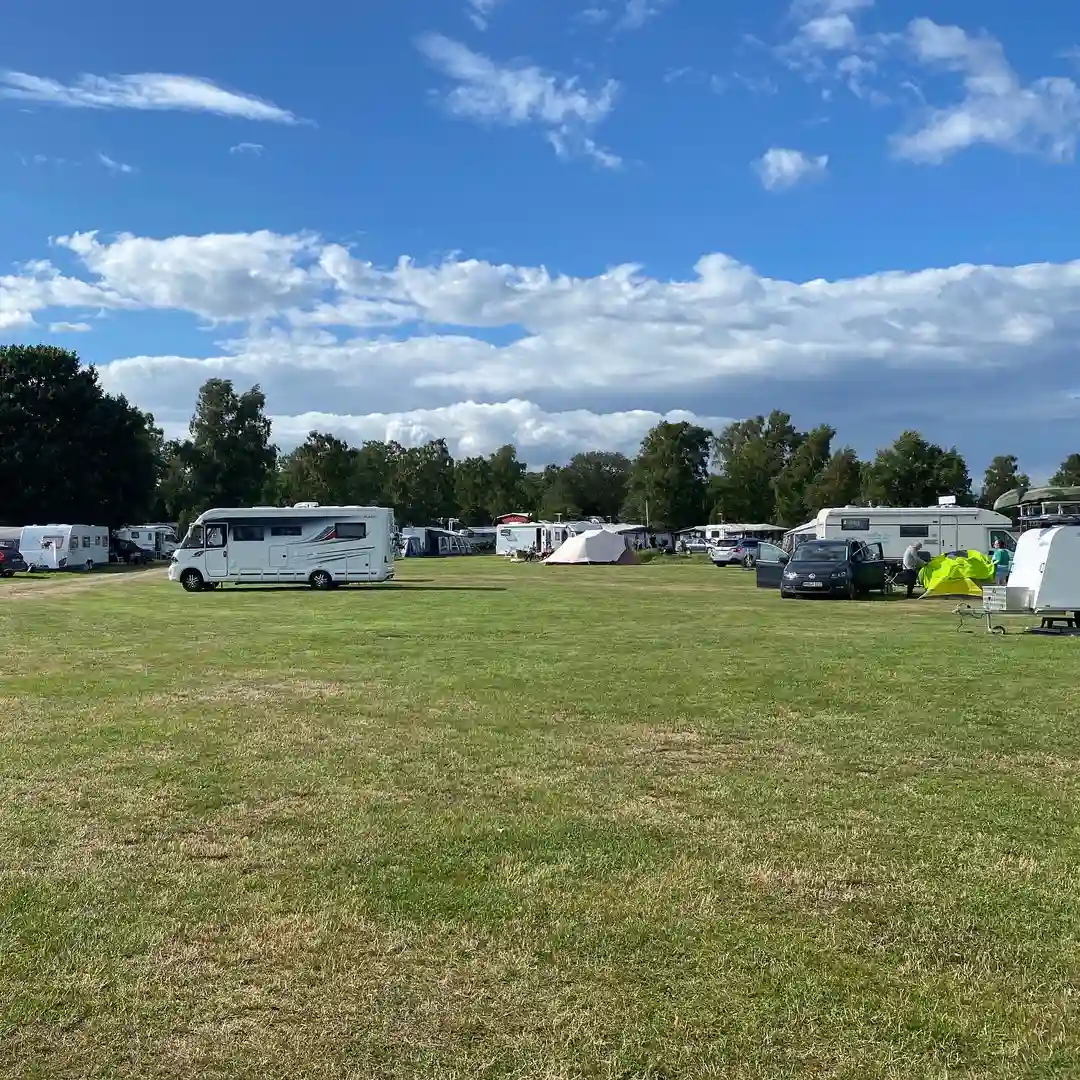 En husvagn parkerad på en grön gräsmatta under en molnig himmel vid Björkenäs camping.