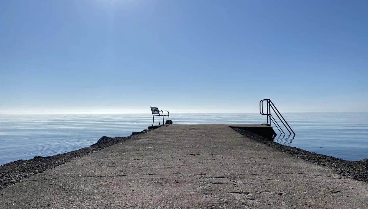 Bilden visar det blåa vattnet vid Björkenäs Camping under en klar himmel. Havshorisonten syns i fjärran, och det är dagtid med lugnande kustlandskap.