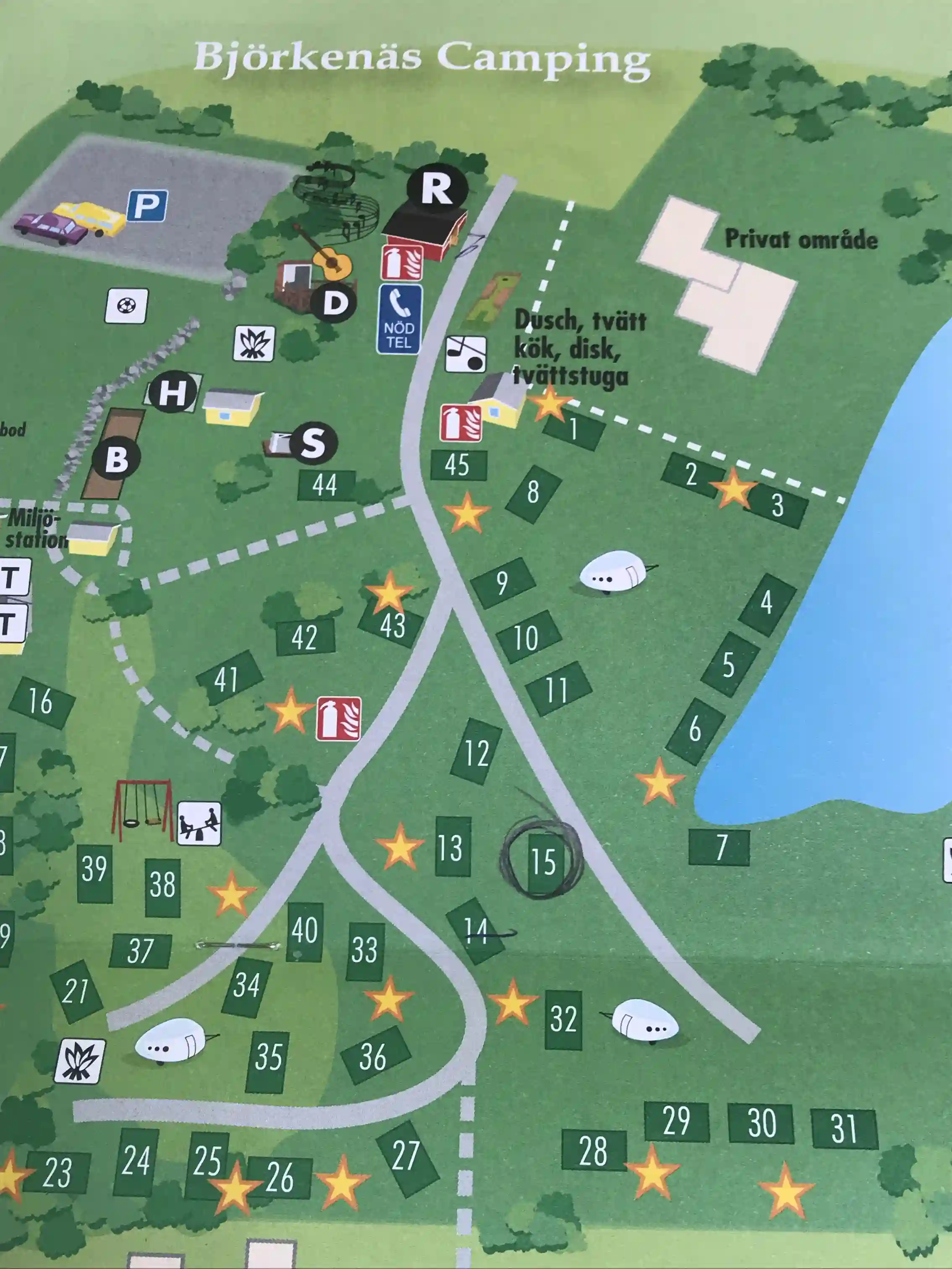 En lugn campingplats omgiven av grönskande skog och öppna ytor, med tält och husvagnar utspridda på gräset.