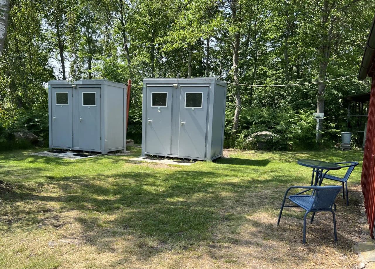 En välordnad trädgård med ett litet skjul och ett uthus vid björkenäs camping. Trädgården är omgiven av gröna växter och erbjuder en lugn atmosfär för besökare.