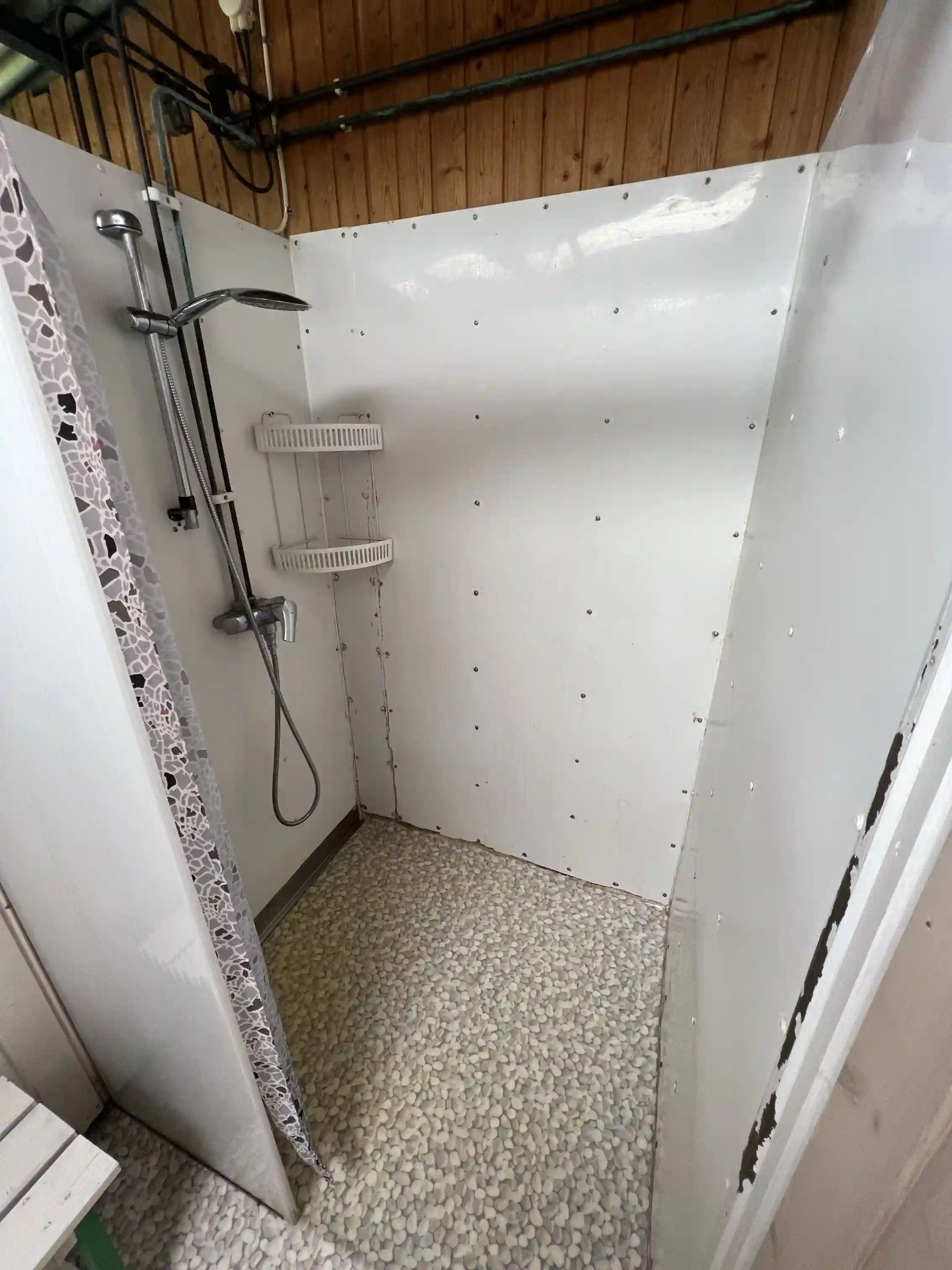 En modern och ren badrumsmiljö med ljusa kakelplattor på golvet och väggarna. En takdusch och moderna VVS-installationer kan ses i bilden, vilket bidrar till en inbjudande och funktionell atmosfär som erbjuds på Björkenäs camping.